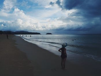 Rear view of woman standing on beach against sky