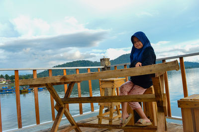 Girl sitting on chair by table against sky,model