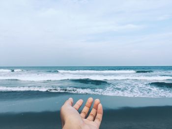 Cropped hand at beach against sky