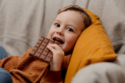 Little adorable boy sitting on the couch at home and eating chocolate bar. child and sweets