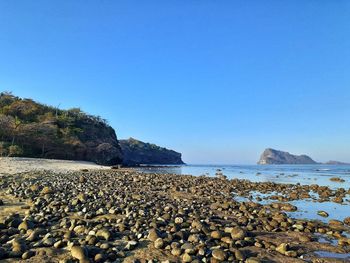 Rocks on beach against clear blue sky