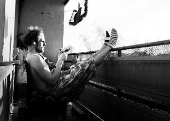 Side view of shirtless mid adult man eating fruit while sitting in balcony