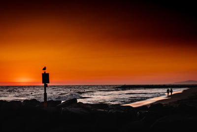 Silhouette people on beach against sky during sunset