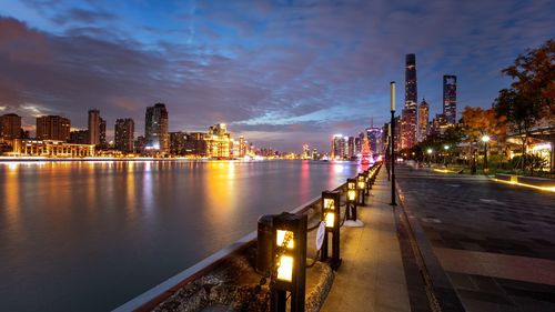 Illuminated buildings by river against sky at night