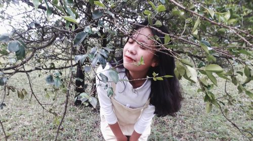 Young woman standing by tree against plants