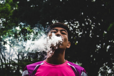 Low angle view of man smoking against trees