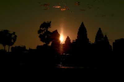 Silhouette trees and buildings against sky at sunset