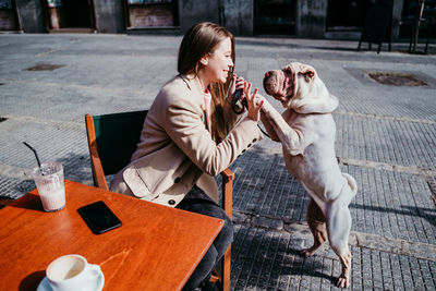 Woman playing with dog while sitting at table in city