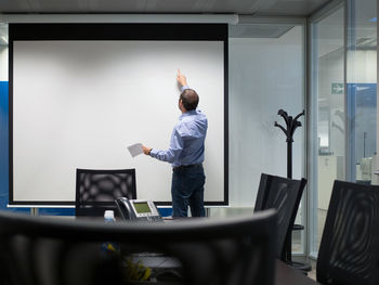 Rear view of businessman standing by projection screen in board room at office