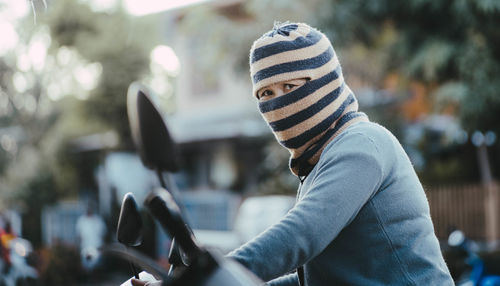 Portrait of woman covering face with knit hat while riding motorcycle