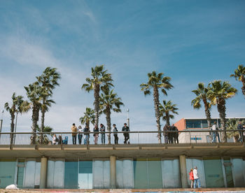 Low angle view of people standing on footbridge in city against sky