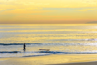 Silhouette man standing on beach against sky during sunset