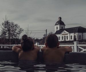 Rear view of friends sitting in swimming pool against buildings