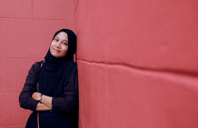 Portrait of smiling young woman standing against wall