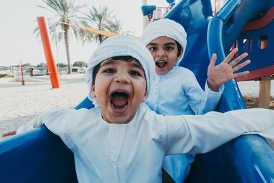 Portrait of happy siblings playing on slide