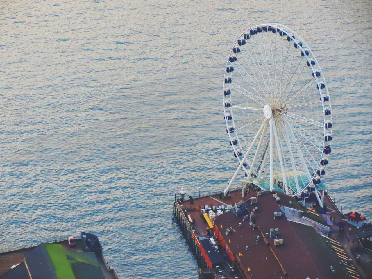 water, ferris wheel, sea, amusement park ride, amusement park, built structure, transportation, high angle view, outdoors, nautical vessel, architecture, waterfront, day, river, rippled, nature, mode of transport, no people, sunlight, arts culture and entertainment