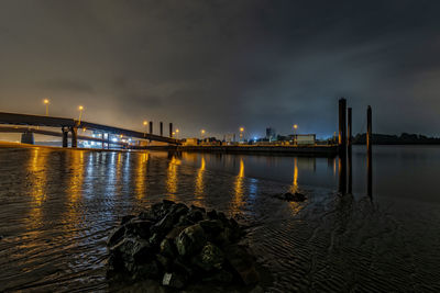 Illuminated bridge over river against sky at night