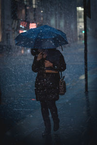 Woman with umbrella walking on wet street during rainy season