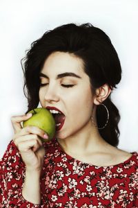 Close-up of young woman eating apple against white background