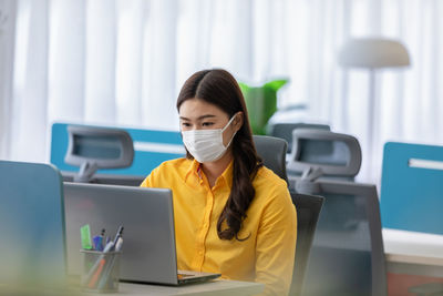 Woman wearing mask while sitting by laptop at table