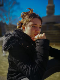 Side view of thoughtful woman looking away while sitting against sky