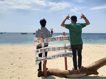 Rear view of men standing at beach against sky