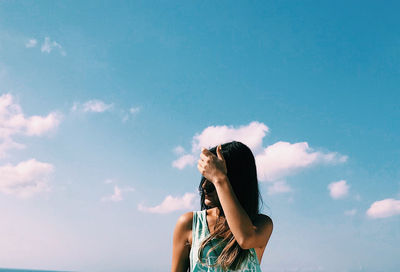 Woman with hand in hair standing against sky