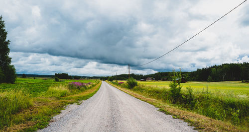 Road amidst field against cloudy sky