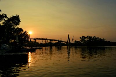 Silhouette bridge over river against sky during sunset