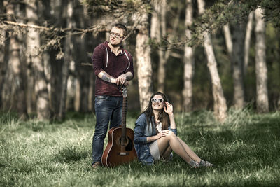 Young couple with guitar against trees in forest