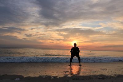 Silhouette teenage boy on beach against sky during sunset
