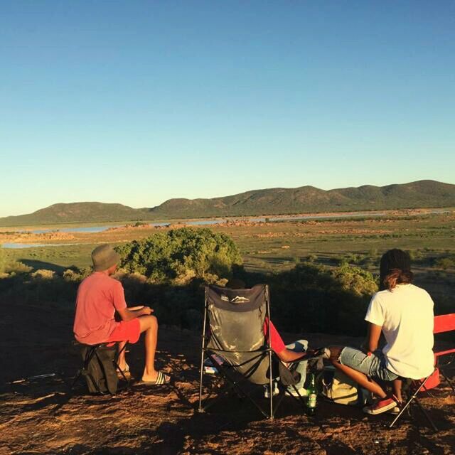 REAR VIEW OF PEOPLE SITTING IN FRONT OF MOUNTAINS