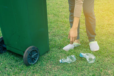 Low section of woman by garbage can picking up crushed plastic bottles on ground