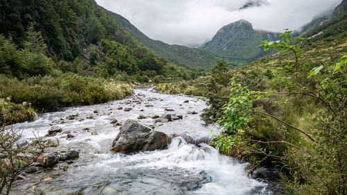 Stream flowing through rocks against sky