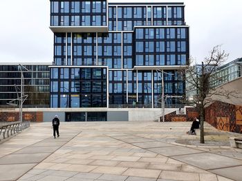 People walking on footpath against modern building in city