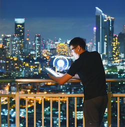 Man using digital tablet while standing in balcony at night