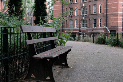 Empty bench and tables in park against buildings in city