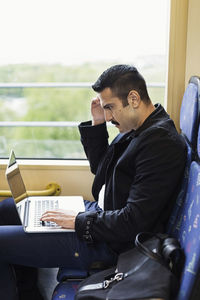 Side view of young man using laptop in tram