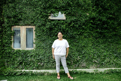 Portrait of woman standing on grassy land against ivy