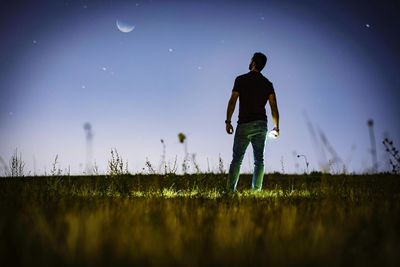 Rear view of man standing on field against sky at night