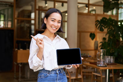 Portrait of young woman using digital tablet while standing in cafe