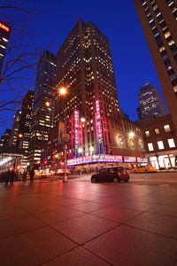 People walking on road against illuminated buildings