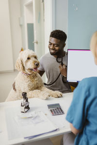 Smiling man with labradoddle looking at female vet in animal hospital