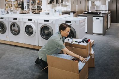 Female retail clerk opening cardboard box while working in appliances store