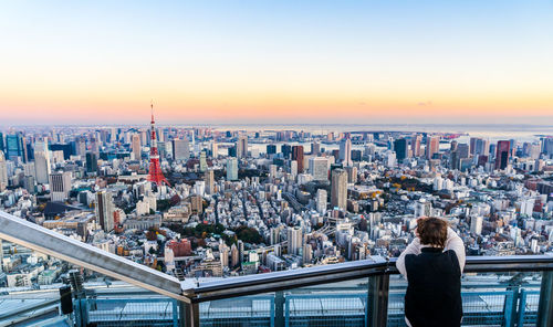 Rear view of woman looking at cityscape during sunset