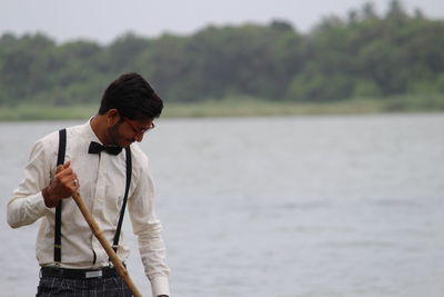 Young man rowing while standing against lake