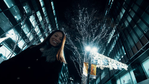 Young woman standing against illuminated building at night