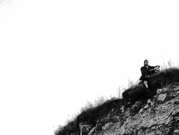 Low angle view of man standing on rock against sky