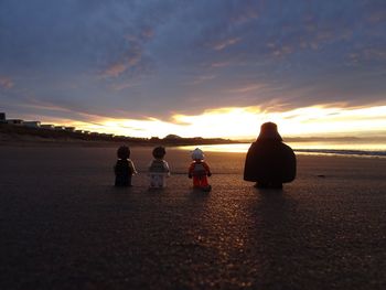 Rear view of people sitting on beach during sunset