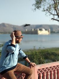 Young man looking at lake against clear sky